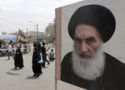 FILE - Shiite pilgrims make their way to the shrine of Imam Moussa al-Kadhim, passing by a poster of Shiite spiritual leader Grand Ayatollah Ali al-Sistani, right, in Baghdad, Iraq, Thursday, May 22, 2014. Iraq’s two rival Shiite political camps remain locked in a zero-sum competition, and the lone voice potentially able to end the rift — the revered Grand Ayatollah Ali al-Sistani — has been conspicuously silent. (AP Photo/Khalid Mohammed, File)