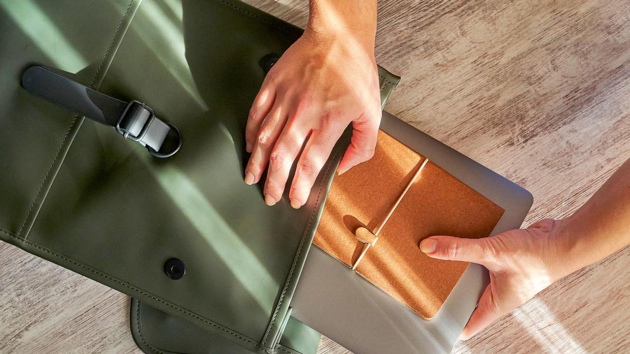 person pulling laptop and notebook out of green bag