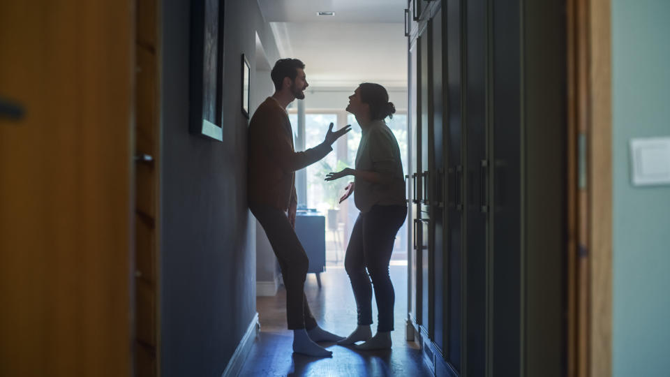 Two people standing and gesturing animatedly in a hallway filled with natural light, engaged in a heated conversation or argument