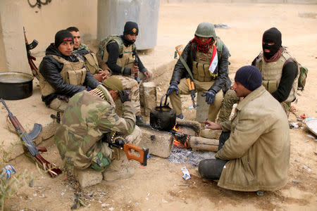 Members of the Lions of the Tigris, a group of Sunni Arab fighters and part of the Hashid Shaabi (Popular Mobilization Comimittee) warm themselves near the fire during a pause in a military operation against Islamic State militants in Shayyalah al-Imam, Iraq November 30, 2016. REUTERS/Thaier Al-Sudani