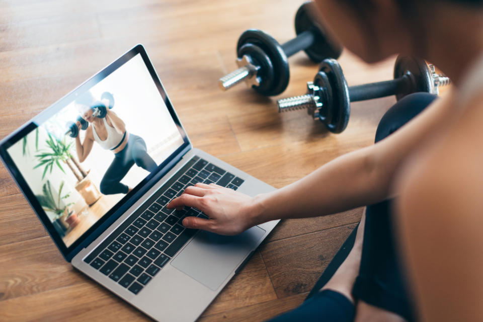 High angle view of young Asian woman practising weight training workout at home with a video lesson on laptop during the day.