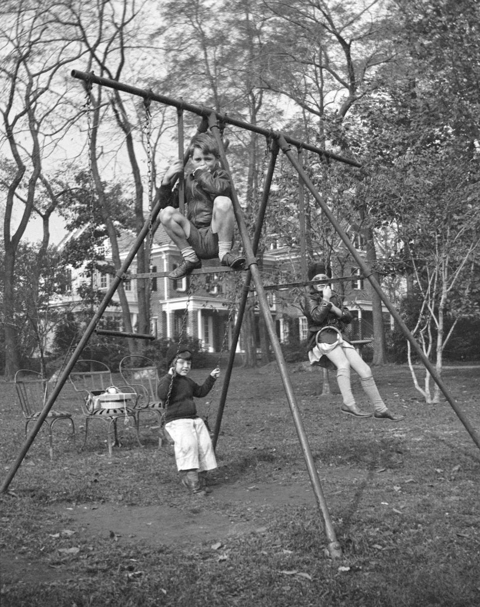 In this October 1934 photo provided by the Kennedy Family Collection, courtesy of the John F. Kennedy Library Foundation, Robert F. Kennedy, top front, Edward M. Kennedy, left rear, and Jean Kennedy, right rear, play on a swing set in Bronxville, N.Y. The Boston-based museum completed an 18-month project in 2018 to catalog and digitize more than 1,700 black-and-white Kennedy family snapshots that are viewable online, giving a nation still obsessed with "Camelot" a candid new glimpse into their everyday lives. (Kennedy Family Collection/John F. Kennedy Library Foundation via AP)
