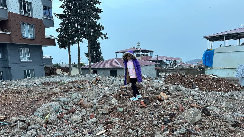 Sengul Karabas, now 7, stands on what remains of their former home in Islahiye. She lost her mother and brother when the building collapsed in the earthquake. - Scott McLean/CNN