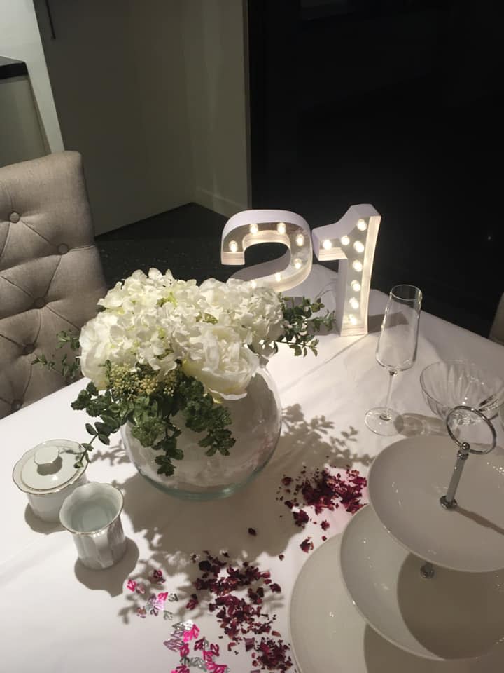 A table decorated with a light-up number 21 and faux flowers in vases