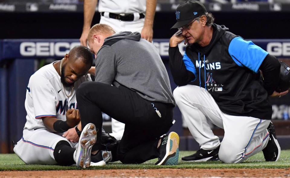 Miami Marlins’ Bryan De La Cruz, left, gets his elbow examined by the training staff as Marlins’ manager Don Mattingly, right, looks on during the fourth inning of a baseball game, Tuesday, May 17, 2022, in Miami.