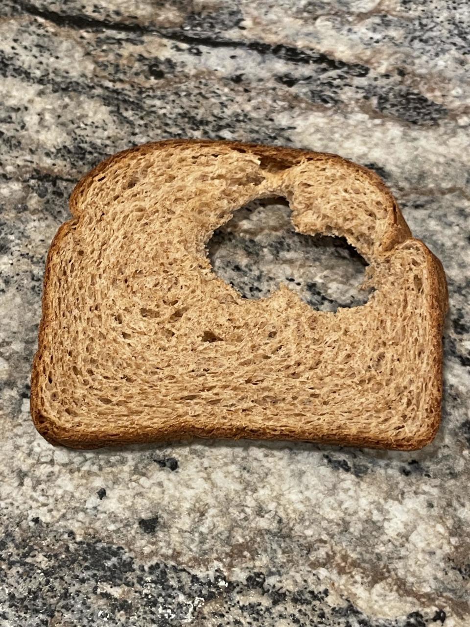 Slice of bread with a large bite taken from the center, placed on a granite surface