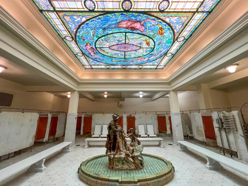 A bathhouse with a stained-glass ceiling and a fountain in the middle of the room.