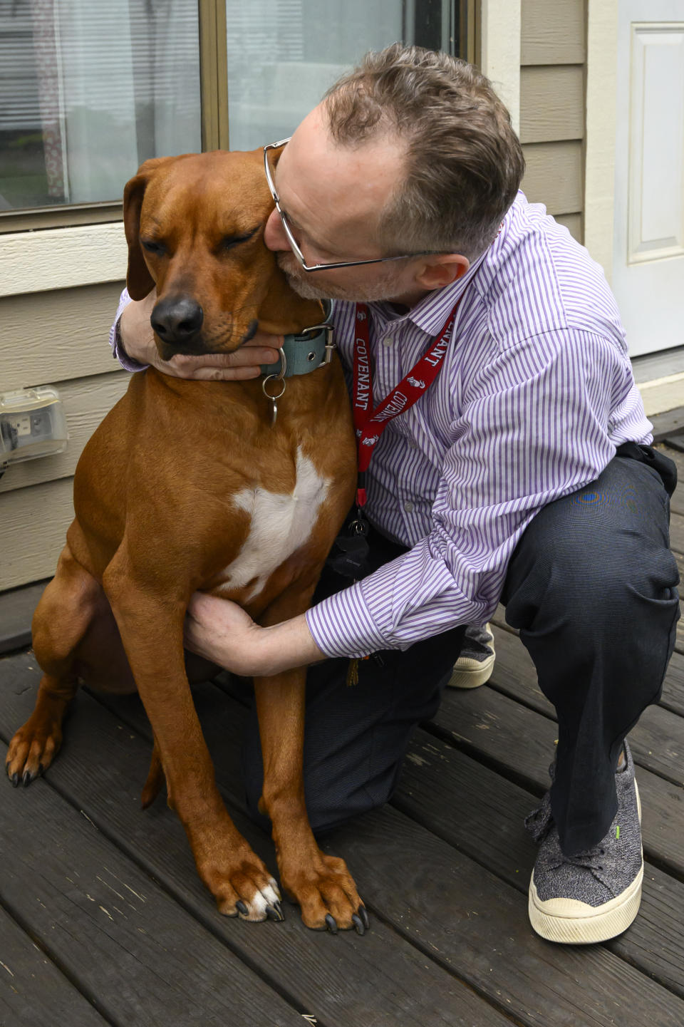 Chaplain Matthew Sullivan spends time with his dog Hank after coming home from work at The Covenant School Friday, March 22, 2024, in Nashville, Tenn. Nearly a year after a shooting at the christian elementary school that left six dead, many of the school's families have adopted dogs in dealing with their shared suffering. (AP Photo/John Amis)