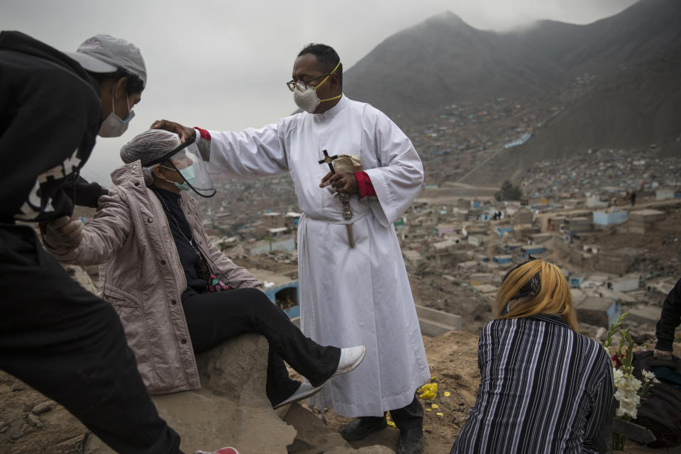 El hermano Ronald Marín, un laico de Venezuela, traza una pequeña cruz en la frente de Aurora Dávila durante el funeral de su hijo de 35 años que murió por el nuevo coronavirus, en el cementerio "Mártires 19 de Julio" en Comas, en las afueras de Lima, Perú, el sábado 4 de julio de 2020. En un momento en que las autoridades peruanas calculan que más de una cuarta parte de la población de Lima pudo haber sido infectada con el nuevo coronavirus, Marín es uno de los pocos representantes de la Iglesia católica que permanece en cementerios junto a los dolientes. (AP Foto/Rodrigo Abd)