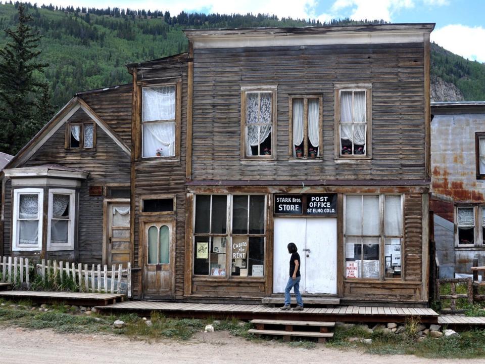 a dilapidated building in st elmo, colorado, with a person walking across the porch