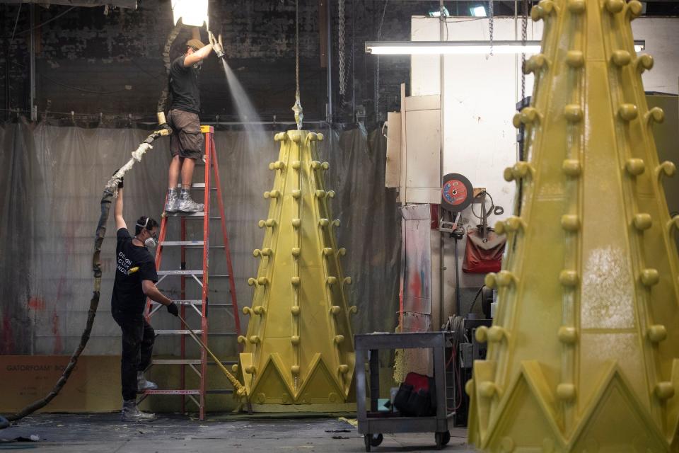 Prop Art Studio sculptors Dusty Conley sprays urethane hard shell coatings onto a Mariners' Church spires as co-worker Ryan Wheeler spins the spires at the studio in Detroit on Thursday, June 28, 2023.