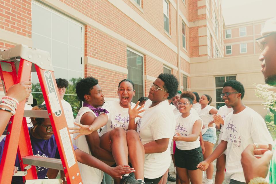 11th-grade students participating in a trust fall from a ladder at the Bridge Builders summer leadership conference.