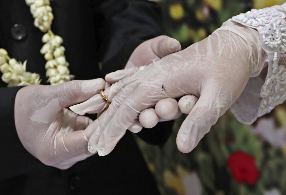 FILE - Wearing latex gloves to prevent the spread of the coronavirus, a bride and groom exchange rings during their wedding ceremony at the local Religious Affairs Office in Pamulang, on the outskirts of Jakarta, Indonesia, on June 19, 2020. Now that weddings have slowly cranked up under a patchwork of ever-shifting restrictions, horror stories from vendors are rolling in. Many are desperate to work after the coronavirus put an abrupt end to their incomes and feel compelled to put on their masks, grab their cameras and hope for the best. (AP Photo/Tatan Syuflana, File)