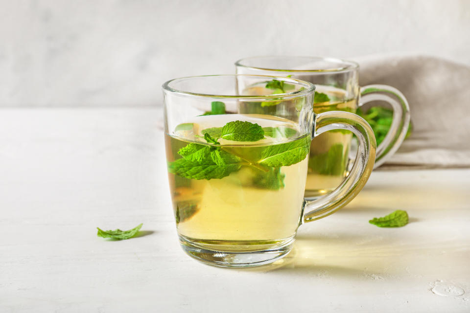 Mint tea in clear glass cups on white wooden table on white background.