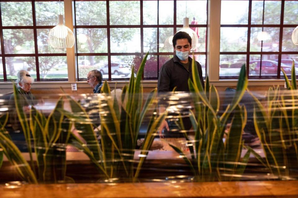 Server Ricky Jacquez waits on customers seated at a booth — with plastic wrap above a short wall providing an additional separation from customers in nearby booths — during Brookfields Restaurant’s second day of dine-in service Friday, May 15, 2020, in Roseville. Placer County was among the first in California to be authorized to reopen certain brick-and-mortar sectors of the economy.