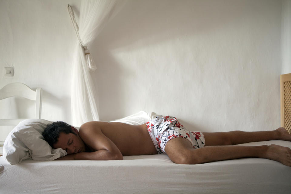 Person resting on a bed with white linens, head on pillow, wearing patterned shorts