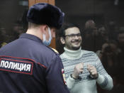 Russian opposition activist and former municipal deputy of the Krasnoselsky district Ilya Yashin gestures, smiling as he stands inside a glass cubicle in a courtroom, prior to a hearing in Moscow, Russia, Friday, Dec. 9, 2022. Yashin faces a trial on charges stemming from his criticism of the Kremlin's action in Ukraine. (Yury Kochetkov/Pool Photo via AP)