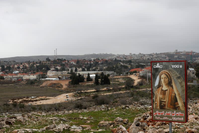 A sign for a Palestinian clothing shop is seen in the village of Silwad as the Jewish settlement of Ofra appears in the background, near Ramallah in the Israeli-occupied West Bank