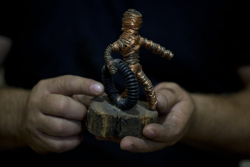 In this Saturday, Nov 2, 2019 photo, Palestinian artist Haitham Khateeb holds his sculpture depicting a protester with a tire, at his house in the West Bank village of Bilin near Ramallah. After 14 years as a photographer in the Israeli-occupied West Bank, Khateeb has found his second calling through sculpture, telling stories by recycling metal wire into art. (AP Photo/Majdi Mohammed)