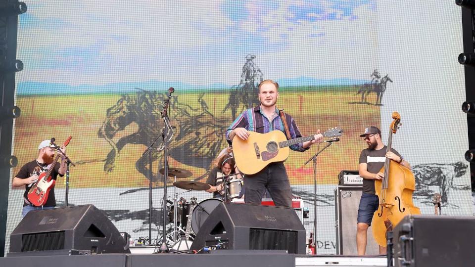 zach bryan playing a guitar while on stage at a festival