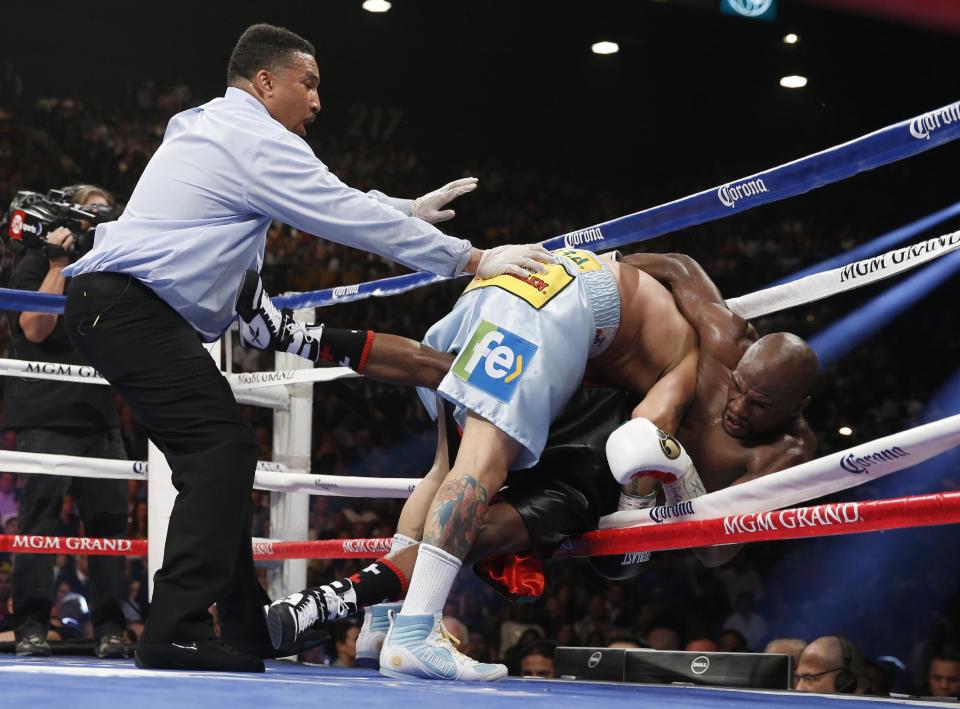 Marcos Maidana, center, from Argentina, knocks Floyd Mayweather Jr. through the ropes in their WBC-WBA welterweight title boxing fight Saturday, May 3, 2014, in Las Vegas. At left is referee Tony Weeks. (AP Photo/Eric Jamison)