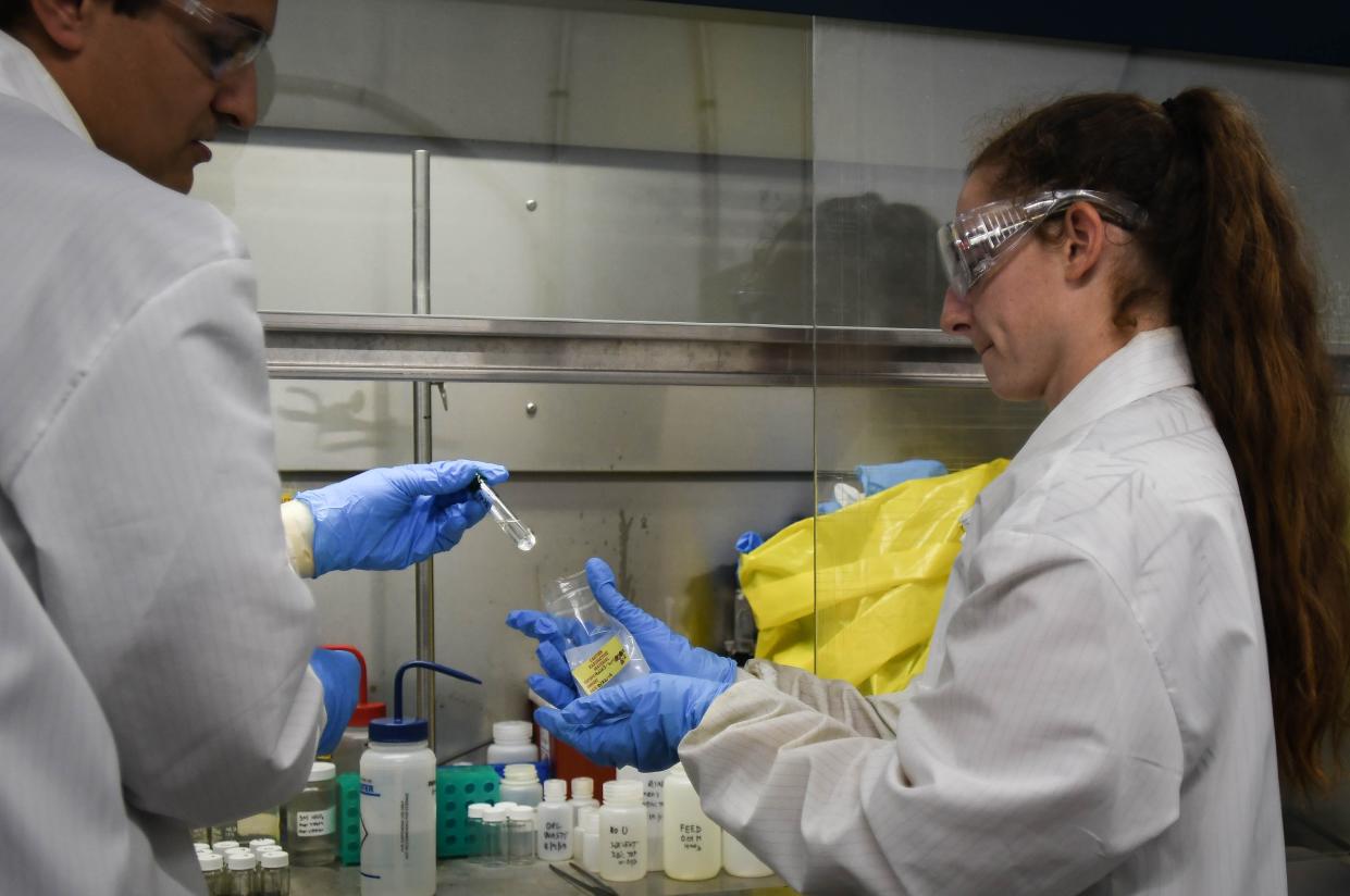 Radiochemist Milan Stika, left, hands a uranium sample to fellow chemist Christine Krizmanich Aug. 22, 2019, in the radiochemistry lab at Niowave in Lansing.