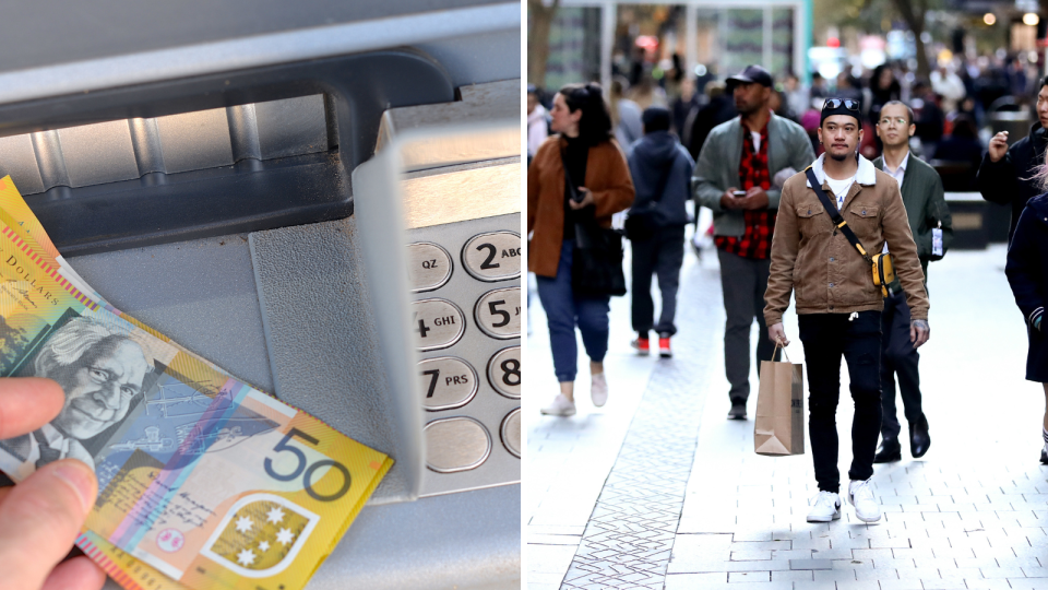 A person holding $50 notes with an ATM in the background and people walking on a busy CBD street.