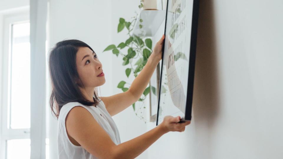 young woman hanging picture frame on wall