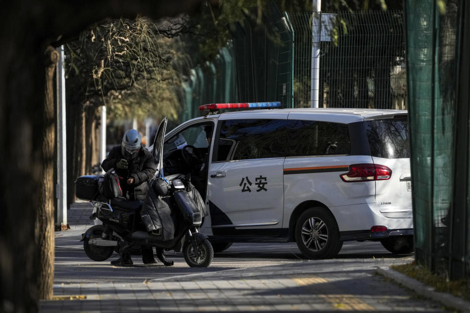 A delivery driver stands near a policeman keeping watch from inside a vehicle near the site of a weekend protest in Beijing, Nov. 30, 2022. / Credit: Andy Wong/AP