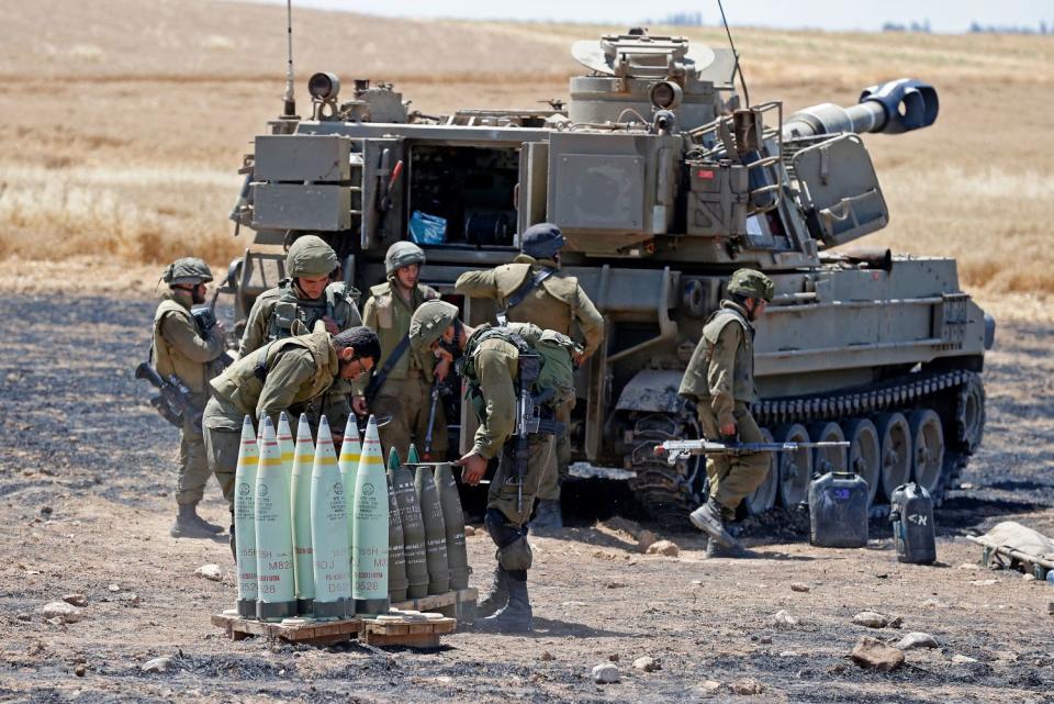 Israeli soldiers stand behind a tank, with artillery shells