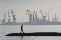 FILE - A man walks with harbor cranes in the background, at the trade port in Mariupol, Ukraine, Feb. 23, 2022. (AP Photo/Sergei Grits, File)