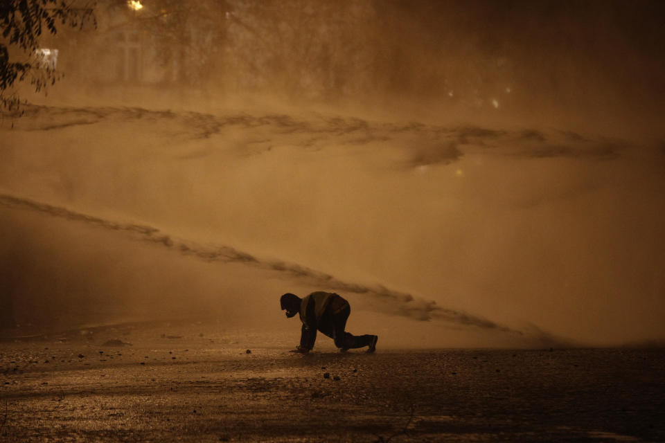 A demonstrator avoids water cannons near the Place de l'Etoile, near the Arc de Triomphe, Saturday, Dec.1, 2018 in Paris. A French protest against rising taxes and the high cost of living turned into a riot Saturday in Paris as police fired tear gas and water cannon in street battles with activists wearing the fluorescent yellow vests of a new movement. (AP Photo/Kamil Zihnioglu)