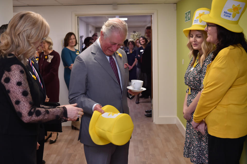 The Prince of Wales is presented with a Marie Curie yellow hat by community fundraiser Hannah Leckie and Hilary James (right) during a visit to the Marie Curie Hospice in Cardiff and the Vale, Wales.