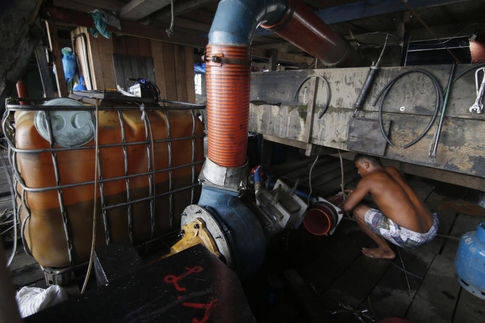 An illegal gold miner fixes a machine on a dredging barge on the Madeira river, a tributary of the Amazon river in Autazes, Amazonas state, Brazil, Thursday, Nov.25, 2021. Hundreds of mining barges have arrived during the past two weeks after rumors of gold spread, with environmentalists sounding the alarm about the unprecedented convergence of boats in the sensitive ecosystem. (AP Photo/Edmar Barros)