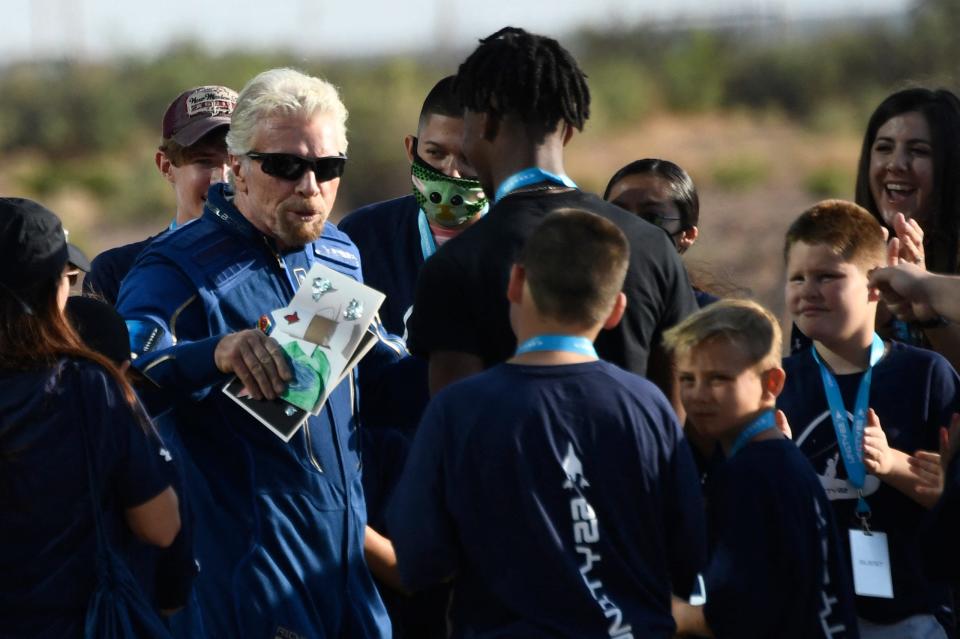 A man is seen in a blue spacesuit receives cards from a crowd of boys.