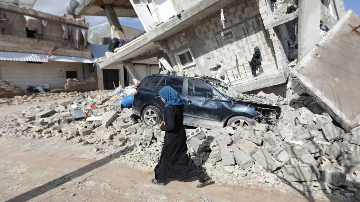 A Syrian woman walks past a half collapsed house in the town of Azaz on the border with Turkey on February 7, 2023, following a deadly earthquake. - The Syrian Red Crescent appealed to Western countries to lift sanctions and provide aid after a powerful earthquake has killed more than 1,600 people across the war-torn country. The 7.8-magnitude quake early the previous day, which has also killed thousands in neighbouring Turkey, led to widespread destruction in both regime-controlled and rebel-held parts of Syria. (Photo by Bakr ALKASEM / AFP)