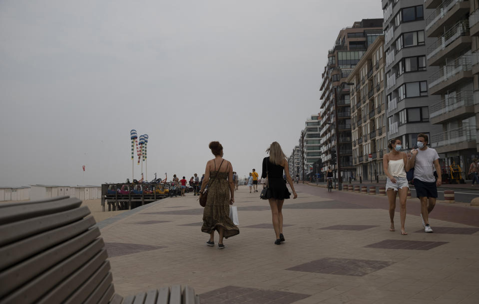 People walk on the promenade along the coastline at the Belgian seaside resort of Knokke, Belgium, Tuesday, Aug. 11, 2020. At the seaside resort of Knokke-Heist, where golf carts with license plates ply well-kept streets, there was ample room to stretch out on the local beach this week. Local authorities have banished day trippers from Belgian cities or France from its 15-kilometer (10-mile) stretch of sands until the heat wave is over. (AP Photo/Virginia Mayo)