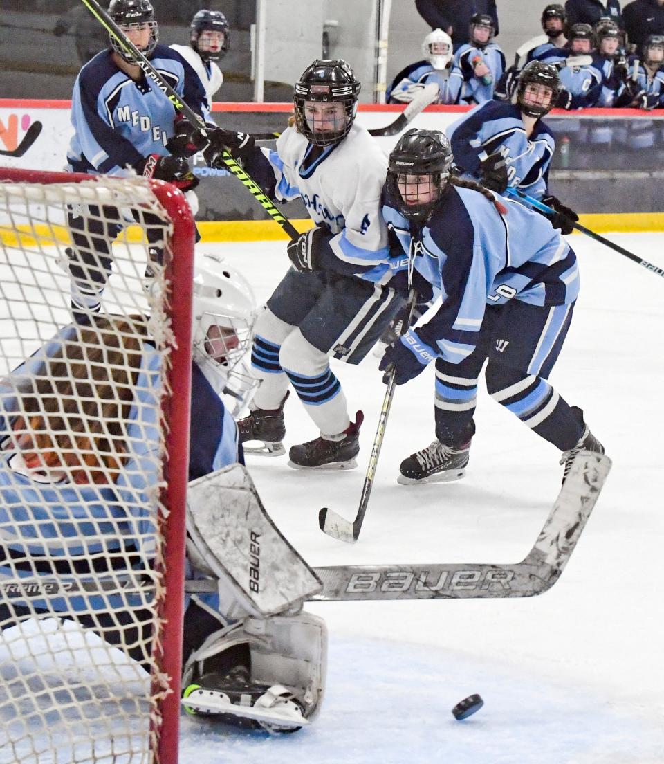 BOURNE -- 03/09/22 -- Marley Dwyer, of Sandwich, and Lily Goodman, of Medfield, watch the shot deflected by Sandwich goalie Sophia Visceglio in the MIAA Division 2 round of 16 girls hockey.