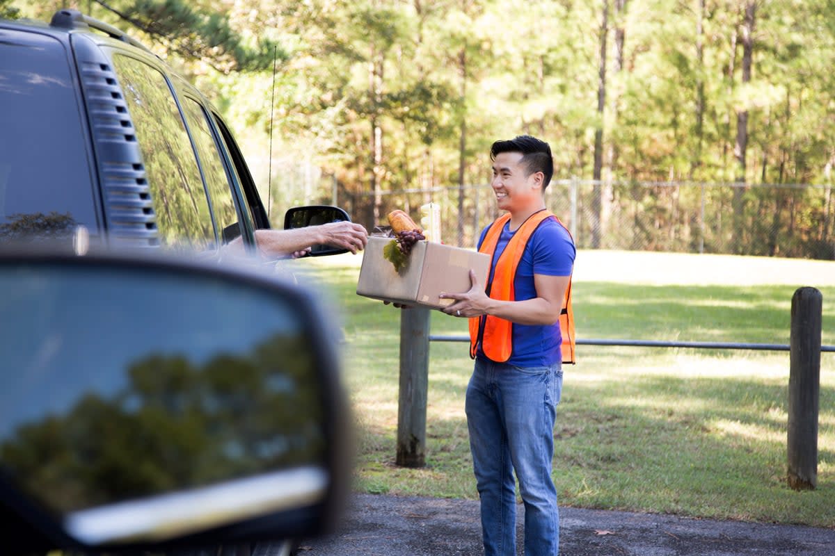 A man hands off a box of food to someone driving a truck.