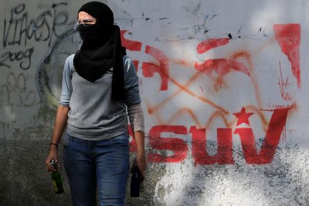 A demonstrator stands next to a graffiti depicting the eyes of Venezuela's late President Hugo Chavez as she holds Molotov cocktails during a strike called to protest against Venezuelan President Nicolas Maduro's government in Caracas, Venezuela July 26, 2017. REUTERS/Marco Bello