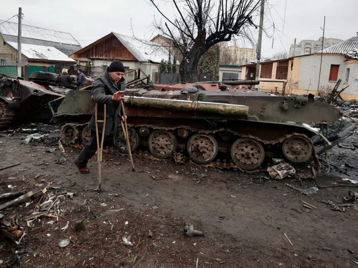 A man on crutches walks past the remains of a Russian military vehicles.