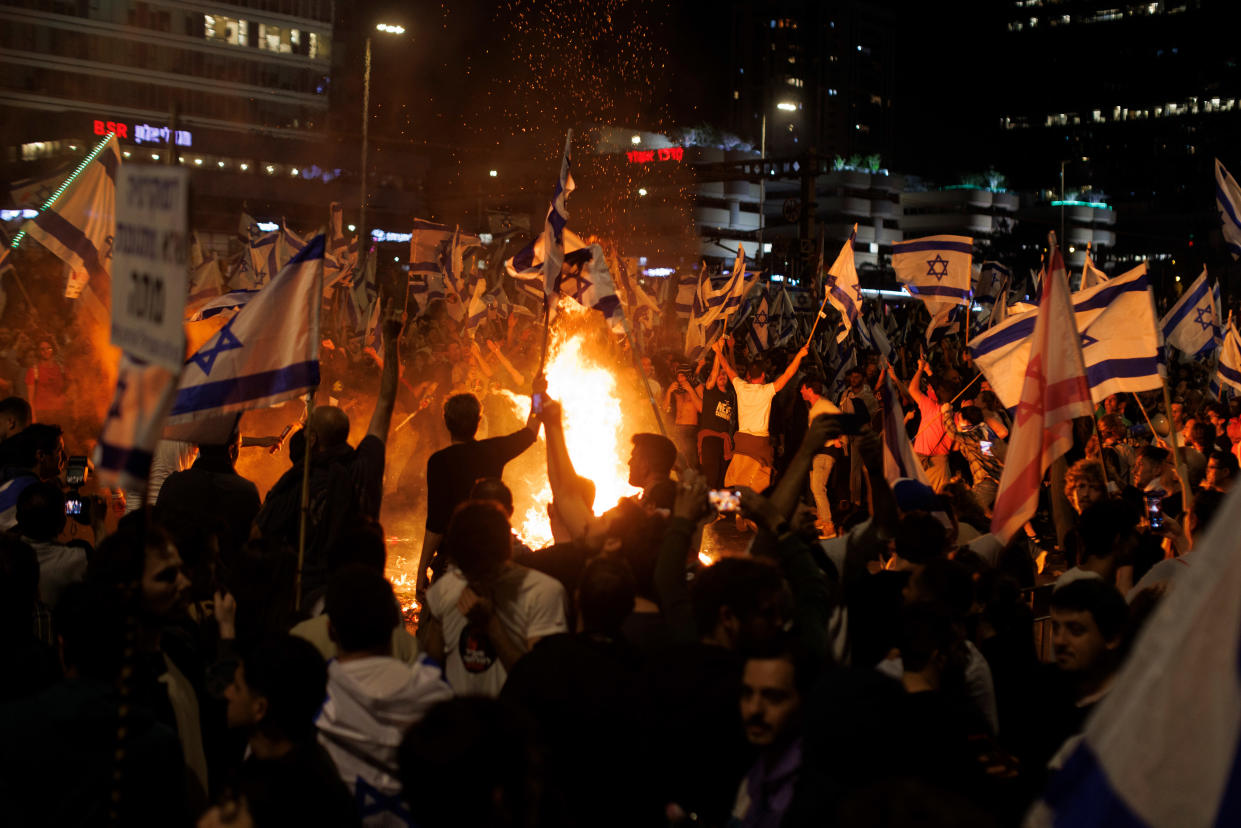 Demonstrators holding Israeli flags surround a bonfire on the road.