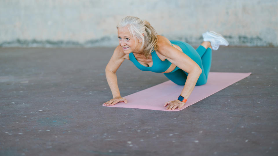 Senior woman in workout gear on a yoga mat performing a push-up outside