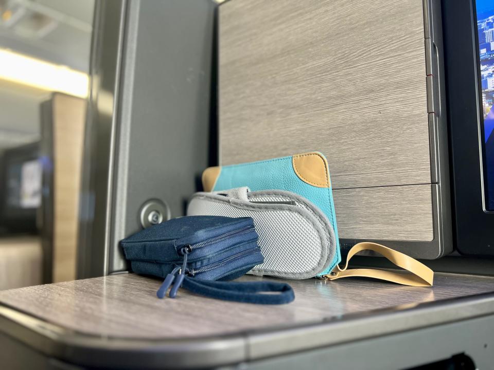 An amenity kit, a blue pouch, and slippers on the side table in "The Room."