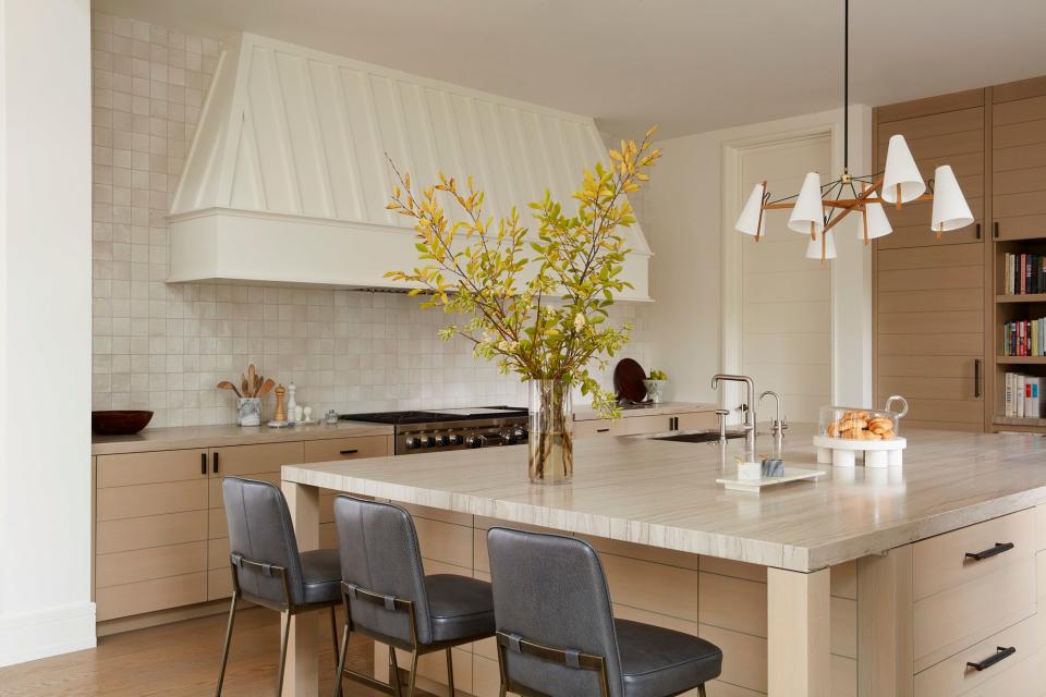 The soothing kitchen comes to life by way of an Ann Sacks tile backsplash and a Brendan Ravenhill Long Hood Chandelier. Three Lawson-Fenning Elysian barstools sit along the kitchen island.