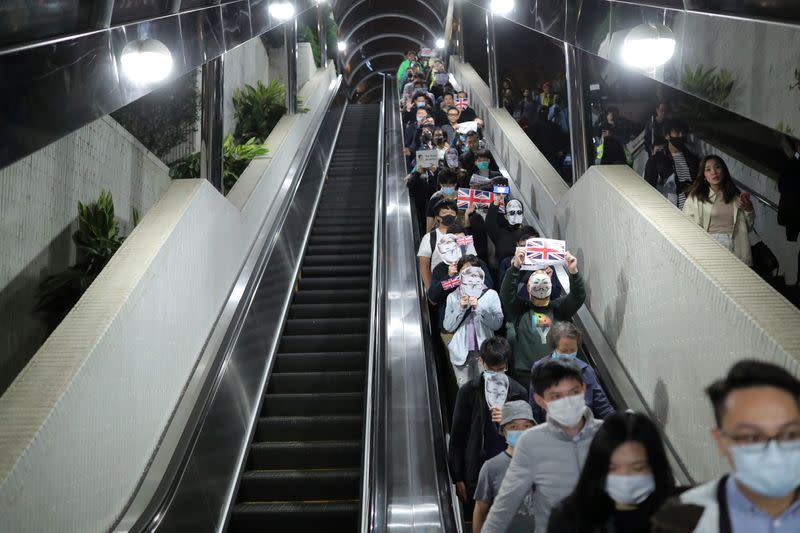 Anti-government protesters wearing masks depicting Simon Cheng, a former British Consulate employee, ride an escalator at a shopping mall during a rally in Hong Kong