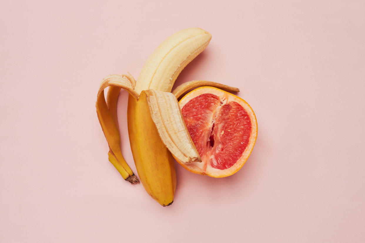 Studio shot of a banana and grapefruit in a suggestive position against a pink background