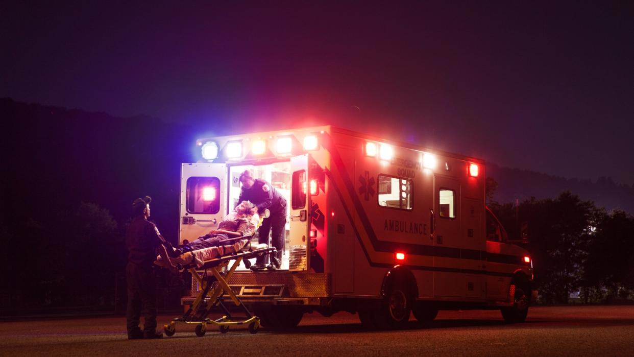 Two paramedics carry a patient on a gurney into an ambulance at night