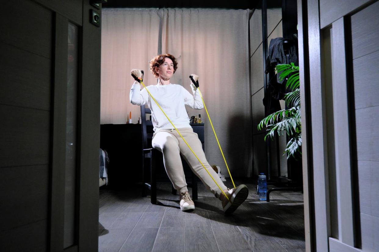 mature woman is exercising at home using chair and resistance band