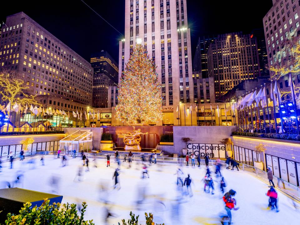 Ice skating rink surrounded by a lit up tree and buildings.